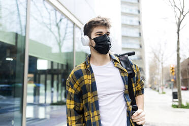 Junger Mann mit Schutzmaske, der einen Elektroroller trägt - RFTF00077