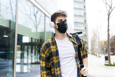 Young man wearing protective face mask while carrying an electrical scooter - RFTF00077