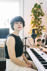 Female musician sitting with electric piano at studio - DGOF02163