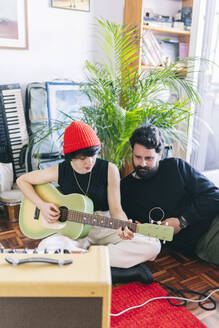 Weiblicher Gitarrist spielt Gitarre und sitzt neben einem männlichen Komponisten im Studio - DGOF02180
