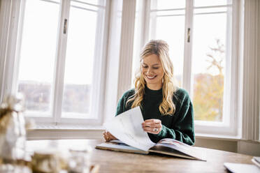 Smiling female freelancer looking at photo album in office - DAWF01972