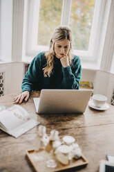 Businesswoman with hand on chin using laptop at office - DAWF01977