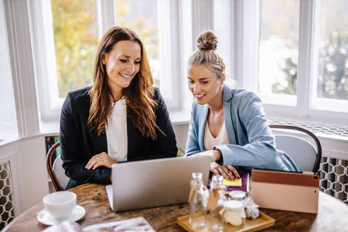 Businesswomen discussing over laptop at office - DAWF01983