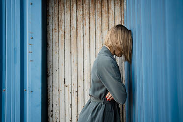 Mittlere erwachsene Frau mit verschränkten Armen, die sich auf einen blauen Fensterladen stützt - RCPF00970