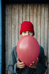 Mittlere erwachsene Frau hält roten Luftballon vor Wellblech - RCPF00980
