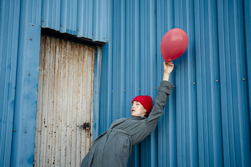 Woman holding balloon while bending over backwards on blue shutter - RCPF00984