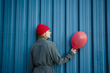 Mid erwachsene Frau hält roten Ballon durch blaue Blende - RCPF00986
