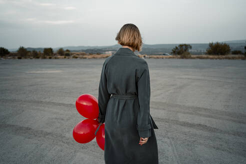 Mittlere erwachsene Frau, die einen Luftballon hält und an der Straße steht - RCPF01004