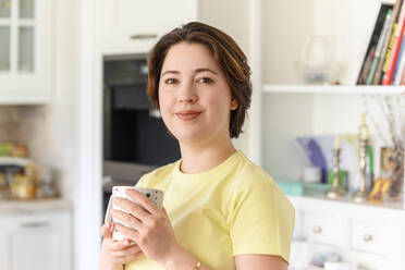 Beautiful woman with short hair holding coffee cup at home - EYAF01592