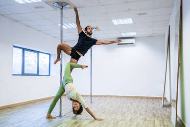 Männliche und weibliche Tänzer dehnen sich beim Üben an der Stange im Tanzstudio - DLTSF01813