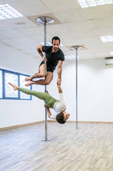 Male acrobat supporting woman while holding hands during rehearsal on rod in dance studio - DLTSF01814
