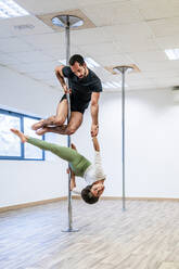 Multiethnische männliche und weibliche Akrobaten üben gemeinsam an einer Stange im Tanzstudio - DLTSF01815