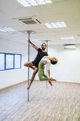 Male acrobat carrying female dancer while hanging on rod in dance studio - DLTSF01817