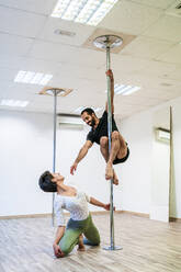Female dancer looking at male acrobat practicing on rod in dance studio - DLTSF01818