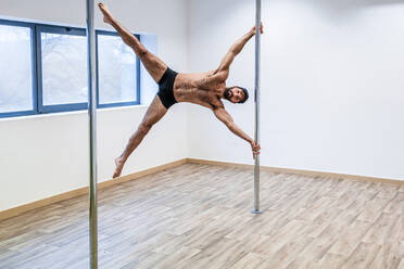 Männlicher Akrobat ohne Hemd balanciert auf einer Stange im Tanzstudio - DLTSF01819