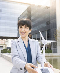 Lächelnde Geschäftsfrau mit Windradmodell im Büropark - JCCMF02043