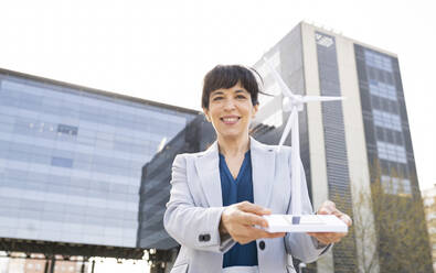 Geschäftsfrau lächelt, während sie ein Windradmodell in der Stadt hält - JCCMF02044