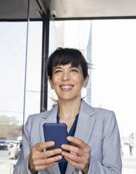 Weibliche Fachkraft lächelt, während sie ein Mobiltelefon am Eingang hält - JCCMF02052