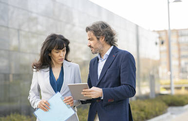 Businessman discussing over digital tablet with female colleague in office park - JCCMF02056