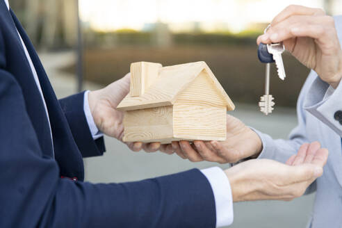 Unternehmerin nimmt Hausschlüssel und Modell von männlichem Immobilienmakler entgegen - JCCMF02075