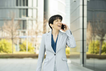 Smiling businesswoman talking on mobile phone in office park - JCCMF02080