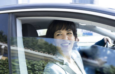 Mature businesswoman smiling while looking through car window - JCCMF02096