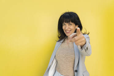 Female entrepreneur pointing while standing in front of yellow wall - JCCMF02100