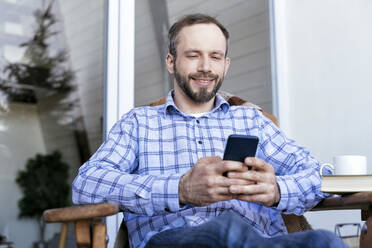 Mann in Freizeitkleidung benutzt Smartphone auf Balkon - OIPF00558