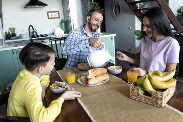 Vater gießt Milch ein, während er mit seiner Familie zu Hause frühstückt - OIPF00567