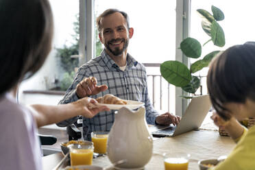 Lächelnder Mann mit Laptop sieht Frau beim Frühstück zu Hause an - OIPF00570