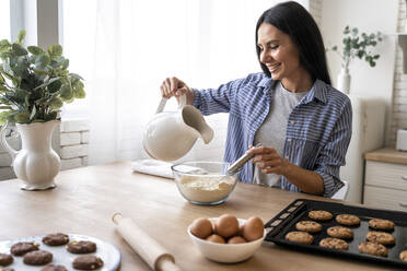 Beautiful woman weighing flour on kitchen scale for baking cake at home  stock photo