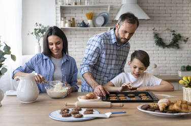 Vater und Sohn betrachten einen Keks, während die Mutter in der Küche zu Hause Mehl mischt - OIPF00592