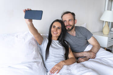 Frau nimmt Selfie mit Mann durch Smartphone auf Bett zu Hause - OIPF00597