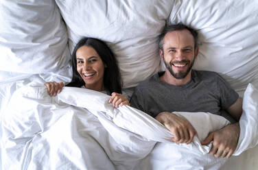 Happy couple with blanket lying on bed at home - OIPF00599