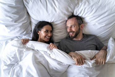 Couple looking at each other while lying on bed with blanket at home - OIPF00600