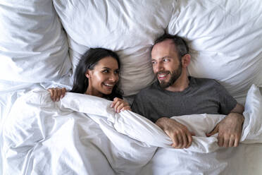 Paar, das sich gegenseitig ansieht, während es zu Hause auf einem Bett mit Decke liegt - OIPF00600