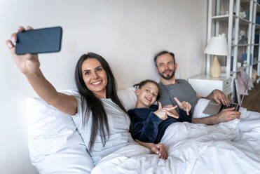 Frau nimmt Selfie mit Familie durch Smartphone auf Bett zu Hause - OIPF00602