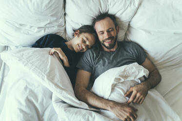 Father and son with blanket lying on bed at home - OIPF00611