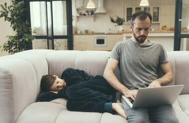 Son sleeping beside father using laptop on sofa at home - OIPF00616