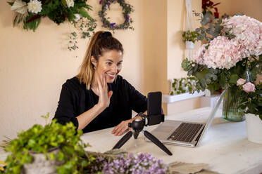 Lächelnde Geschäftsfrau winkt bei einem Videoanruf in einer Werkstatt - MPPF01726