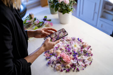 Frau fotografiert Blumen mit ihrem Smartphone bei einem Workshop - MPPF01733