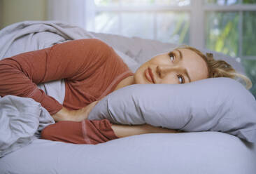 Thoughtful woman lying on bed at home - AZF00296