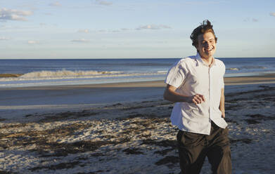 Smiling young man running on beach - AZF00300