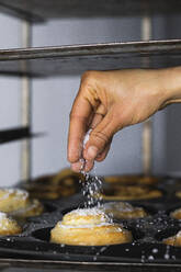 Hand streut Zucker auf Zimtschnecke in der Küche - PNAF01472