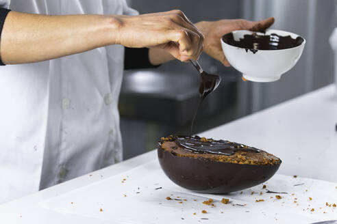 Bäckerin gießt Schokolade auf ein Dessert in der Küche - PNAF01476