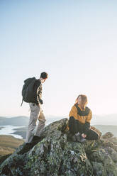 Young female hiker sitting by man standing on top of mountain - RSGF00657