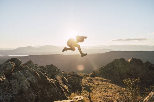 Sportler springt an einem sonnigen Tag auf einen Berg - RSGF00659