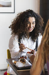 Lächelnde Frau betrachtet ihre Freundin beim Essen im Restaurant - PNAF01502