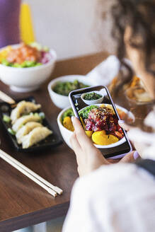 Frau fotografiert Essen im Restaurant mit ihrem Smartphone - PNAF01503