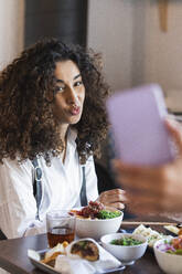Eine Freundin fotografiert eine junge Frau, die in einem Restaurant beim Essen sitzt - PNAF01506